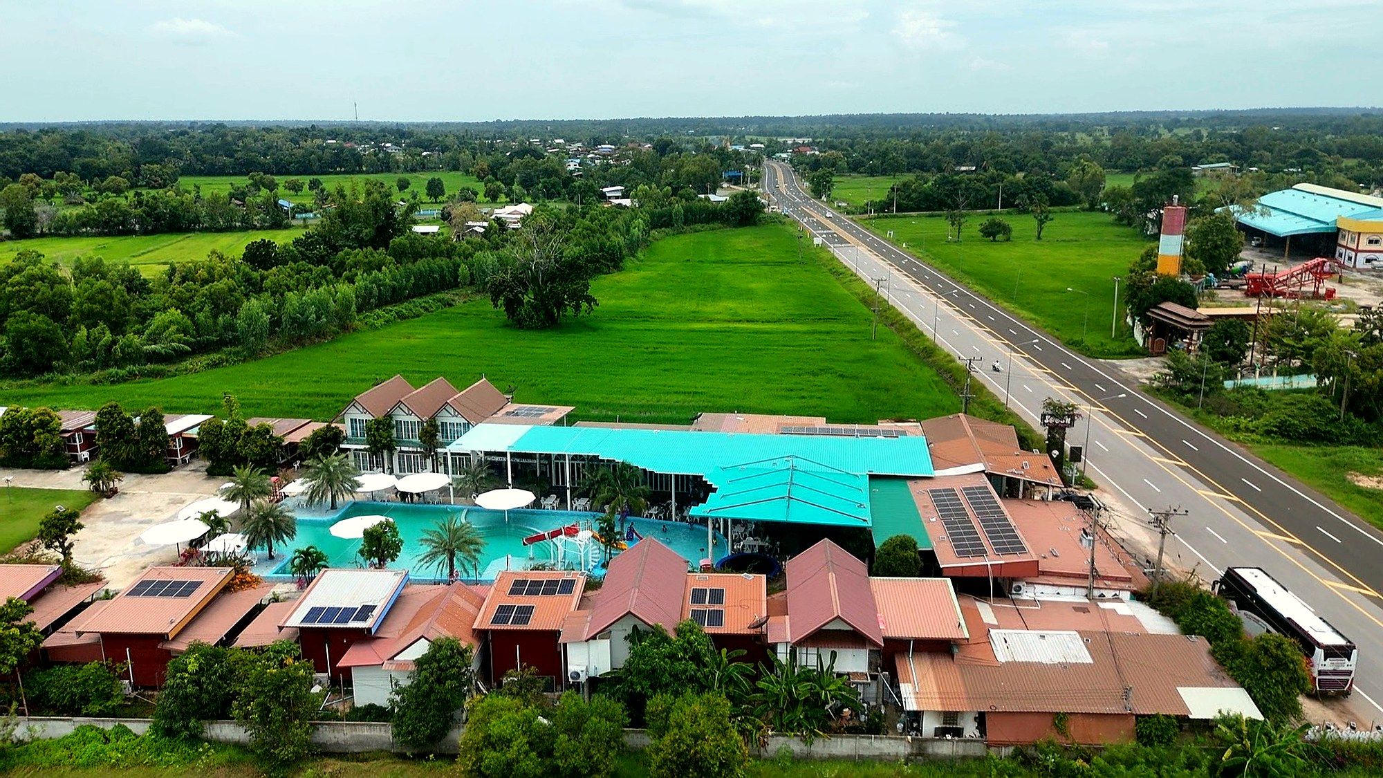 Luftaufnahme des Resorts mit Pool, Häusern und Reisfeldern